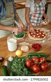 Pizza Day. Cropped Shot Of Couple Making Pizza Together At Home. Man In Apron Adding Basil On The Dough While Woman Adding Mozzarella Cheese. Hobby, Lifestyle. Selective Focus. Vertical Shot