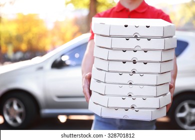 Pizza delivery boy holding boxes with pizza near car - Powered by Shutterstock