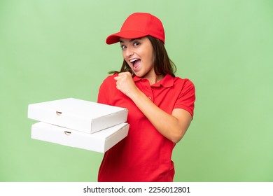Pizza delivery caucasian woman with work uniform picking up pizza boxes isolated on green chroma background celebrating a victory
