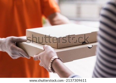 Pizza Delivery. Closeup hands of customer get food delivery from deliveryman in ornage uniform. New normal courrier food service by mobile application to prevent covid-19 omicron pandemic.