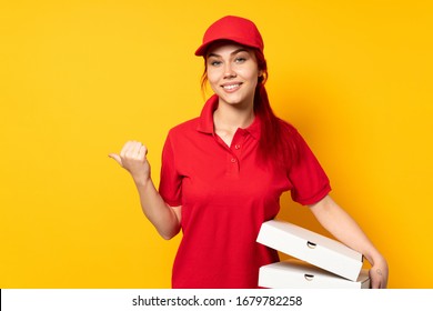 Pizza Delivery Girl Holding A Pizza Over Isolated Background Pointing To The Side To Present A Product