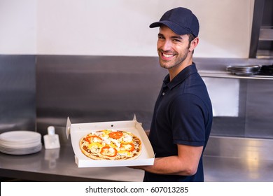 Pizza delivery man showing box in commercial kitchen - Powered by Shutterstock