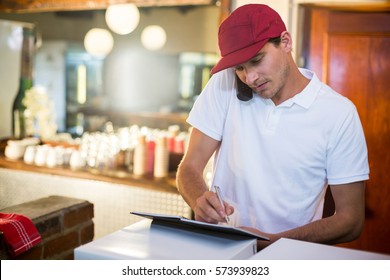 Pizza delivery man taking an order over the phone at counter in restaurant