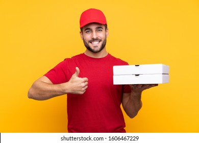 pizza delivery man with work uniform picking up pizza boxes over isolated yellow background with thumbs up because something good has happened