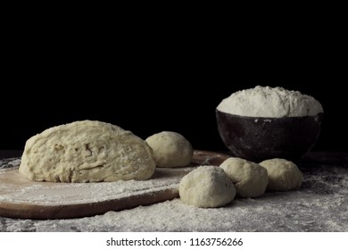Pizza dough cut in portions on cutting board and a bowl with flour baking on dark black background. Baking bread, pizza, pasta. Recipe from chef cooks pizza. Italian home cooking. Horizontal photo