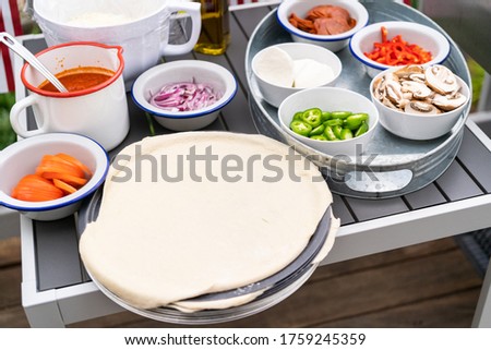 Pizza dough and ingredients for grilling pizza on an outdoor gas grill.