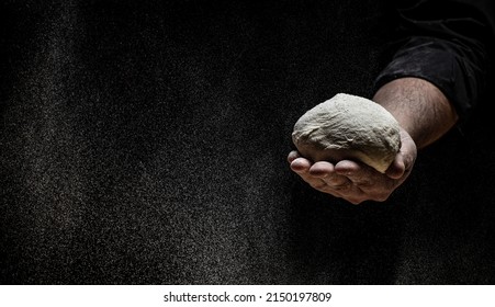 Pizza dough, male hands making dough with flour in a freeze motion of a cloud of flour midair on black with copy space, Long banner format,