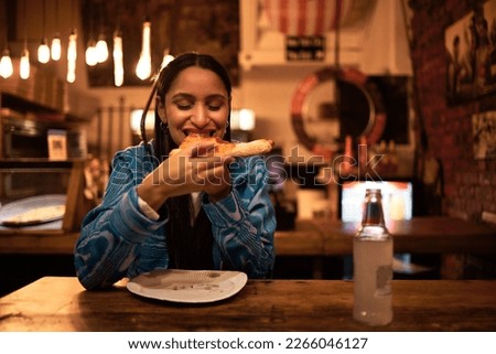 Pizza, food and restaurant where young woman is eating food and enjoying drinks. Hungry female having delicious meal at bar at night. Happy and satisfied foodie having tasty supper at a diner