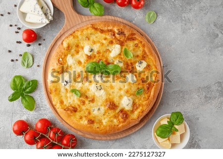 Pizza four cheeses with fresh basil on top on a wooden board on a gray concrete background. Top view, copy space.