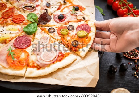 Pizza with ingredients and woman hand on dark background. Food background. Flat lay, top view.