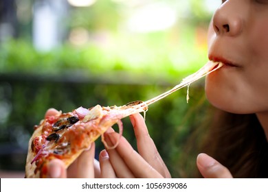 Pizza look so yummy or delicious food. Charming beautiful asia woman is eating pepperoni pizza and sticky mozzarella cheese. Attractive girl feels hungry and loves the taste. She sit at restaurant