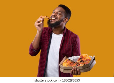 Pizza Lover. Funny Black Man Overeating Junk Food, Eating Slice Of Pizza Posing With Box Over Yellow Studio Background, Smiling To Camera. Unhealthy Nutrition Habits, Cheat Meal Concept