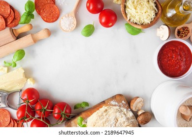 Pizza Making Ingredients Including Cheese, Pepperoni, Tomatoes And Basil. Top Down View Frame Against A White Marble Background. Copy Space.