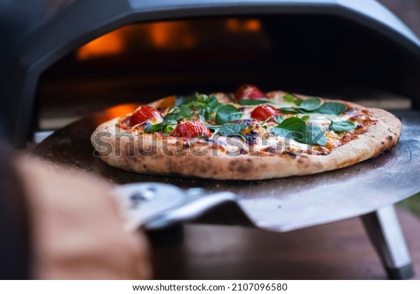 A pizza margarita with fresh\
basil leaves on the background of a gas oven for cooking\
pizza.