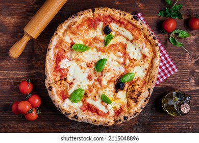 Pizza Napoletana, traditional and authentic Italian pizza baked in wood fired oven. Margherita pizza with mozzarella cheese, tomato sauce, olive oil and basil leaves. On wooden board with ingredients. - Powered by Shutterstock