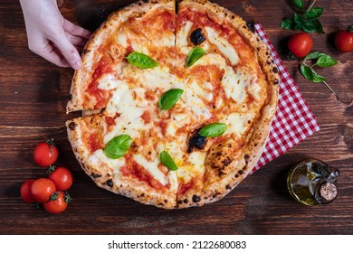 Pizza Napoletana, traditional and authentic Italian pizza baked in wood fired oven. Margherita pizza with mozzarella cheese, tomato sauce, olive oil and basil leaves. On wooden board with ingredients.