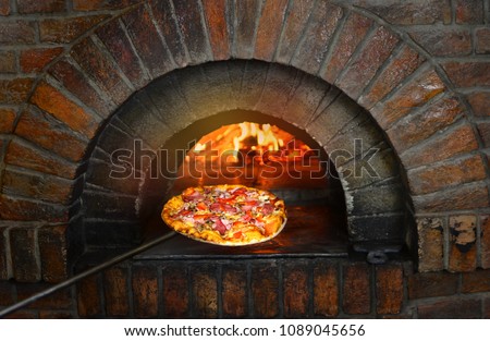 Pizza near the stone stove with fire. Background of a traditional pizzeria restaurant with a fire place. 