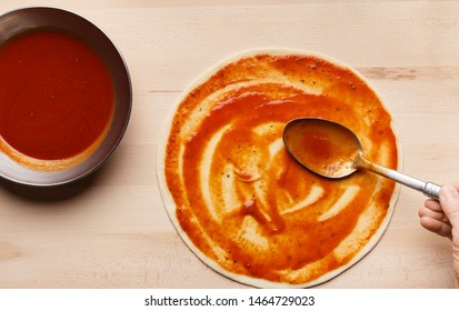 Pizza Preparation. Chef Spreading Tomato Sauce On Pizza Base, Top View