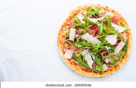 Pizza with prosciutto (parma ham), arugula (salad rocket) and parmesan on white background top view. Italian cuisine. Space for text.
