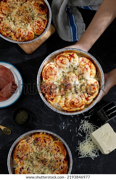 Pizza Roll with Melted Cheese Topping on Round\
Alumunium Baking Pan, Female hand Holding One Pan. Flatlay, Bakery\
Concept