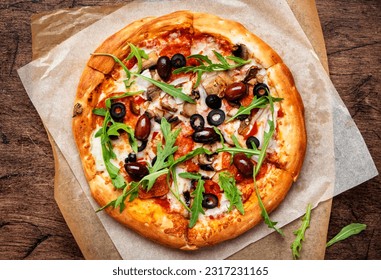 Pizza with salami sausage, mozzarella cheese, mushrooms, black olives, spicy tomato sauce and arugula, rustic wooden table background, top view - Powered by Shutterstock