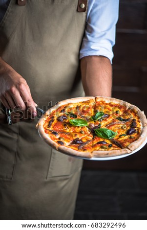 Pizza with seafood in the hands of the chef. Close-up on a dark background. Healthy fresh food. Italian Cuisine.
