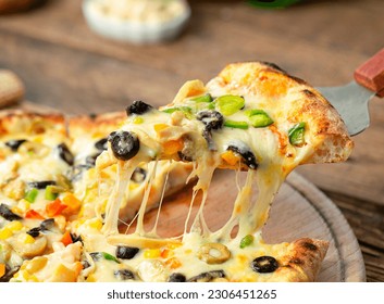 pizza slice with mozzarella cheese and vegetables, baked on a wood-burning oven, with tomato sauce, cheese, corn, olives, sweet peppers and onions, on a wooden background 2 - Powered by Shutterstock