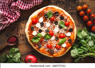 Pizza with tomatoes, mozzarella cheese, black olives and basil. Delicious italian pizza on wooden pizza board. Table top view - Powered by Shutterstock