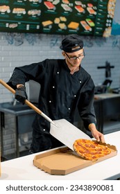 A pizzaiolo pulls a pizza from the oven with a pizza shovel and places it in pizza box in the pizzeria kitchen