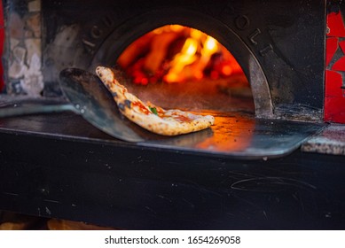 
Pizzaiolo while checking a pizza being cooked in the wood oven with his oven shovel