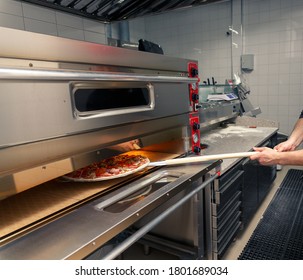 Pizza-jello cook putting pizza in electric oven in a pizzeria, close up
