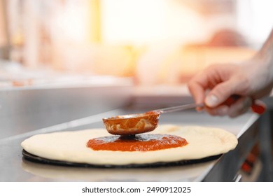 Pizzamaker applies tomato sauce on dough, worker preparing fresh food pizza. Business pizzeria concept. - Powered by Shutterstock