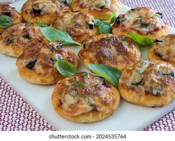 Pizzettas Garnished With Basil Leaves On A White Tray Against A Red And White Table Runner