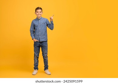Place For Ad. Happy Male Kid Pointing Aside At Copy Space With Hand, Cheerful Teen Boy Advertising Nice Offer Or Advertisement, Standing Against Yellow Studio Background, Full Length Shot