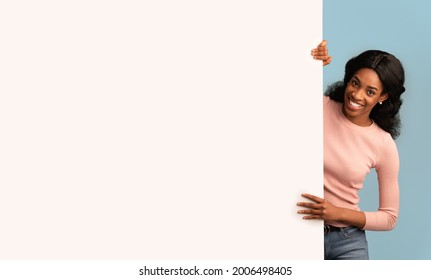 Place For Advertisement. Beautiful Young Black Female Standing Next To Blank Billboard, Smiling African American Woman Demonstrating Copy Space For Your Design Or Offer, Posing Over Blue Background