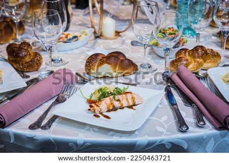 Place setting, cutlery and plate, glasses and napkins table setting ideas. Appetizer first course for meal menu. Fish and meat with salad. Party and wedding food ideas. Orthodox Jewish wedding challah