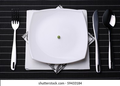 Place Setting Including Silverware And White Plate Filled With One Pea