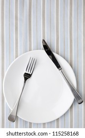 Place Setting On Striped Tablecloth In Shades Of Blue, White And Taupe.  Overhead View.