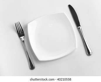 Place Setting For One Person. Knife, Square White Plate And Fork.