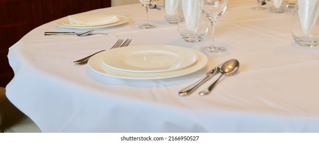 Place setting at round dining table with white linen tablecloth