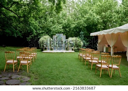 Place for wedding ceremony in garden outdoors, copy space. Wedding arch decorated with flowers and chairs on each side of archway. Wedding setting