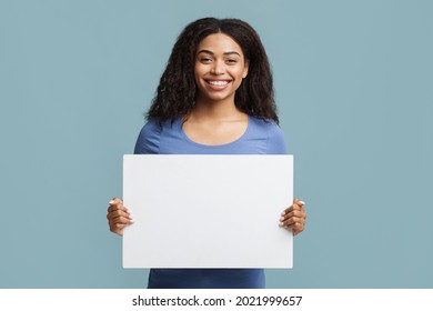 Place for your ad. Cheerful black woman holding blank placard with free space for advertisement or design. African american lady demonstrating white poster, standing over blue background