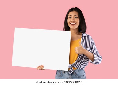 Platz für Ihre Anzeige. Lächelnde asiatische Frau, die leeres leeres Brett hält und Daumen nach oben zeigt Zeichengestalt einzeln auf rosafarbenem Studiohintergrund. Fröhliche Dame, die mit weißem quadratischem Papier für Vorlage steht