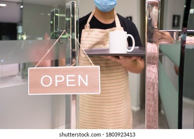 Placing open sign “OPEN” on front door The restaurat Reopening.  man owner with face mask and apron. "Open" on cafe or restaurant hang on door at entrance - Shutterstock ID 1803923413