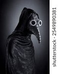 Plague doctor in hooded cloak at night over dark misty background