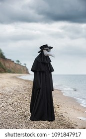 Plague Doctor In Seaside. Outdoor Portrait With Dramatic Sky In Background.