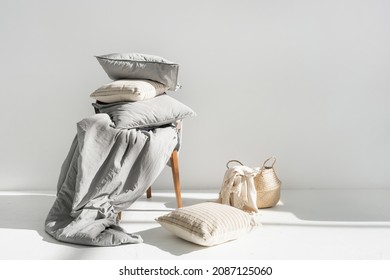 Plaid in wicker basket, clean blanket, linen bedding, cotton sheets, pillow, cushion and duvet with natural material on chair after laundry, copy space. Washing, housekeeping, hotel service concept