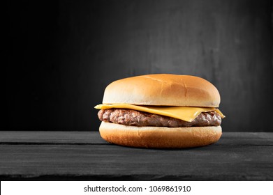 Plain beef burger with cheese on wooden table isolated on black background. - Shutterstock ID 1069861910