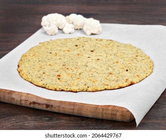 Plain Cauliflower Pizza Crust On A Piece Of Parchment Paper On A Cutting Board.  Selective Focus On Front Edge Of Crust.