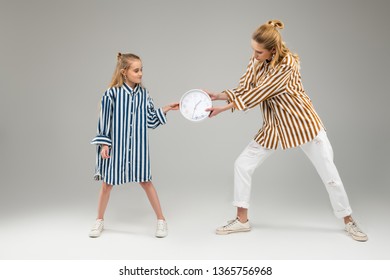 Plain Wall Clock. Long-haired Pretty Sisters Playfully Fighting For Round Clock While Pulling Him Over